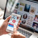 A hand holding a phone with the Pinterest app open on the screen